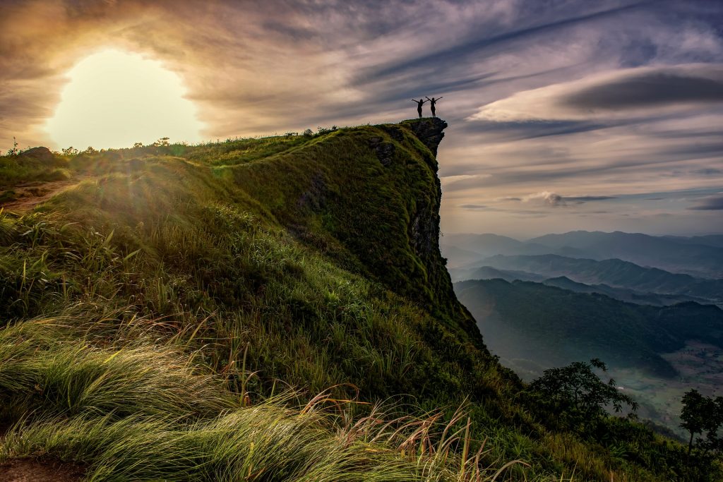 Zwei Menschen stehen im Sonnenuntergang am Rand eines Felsen, der über ein Tal ragt.