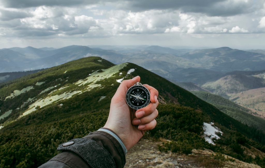 Eine Hand hält einen Kompass vor einem weitläufigen Gebirge.
