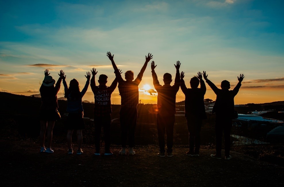 Un grupo de personas estirando los brazos hacia arriba durante la puesta de sol