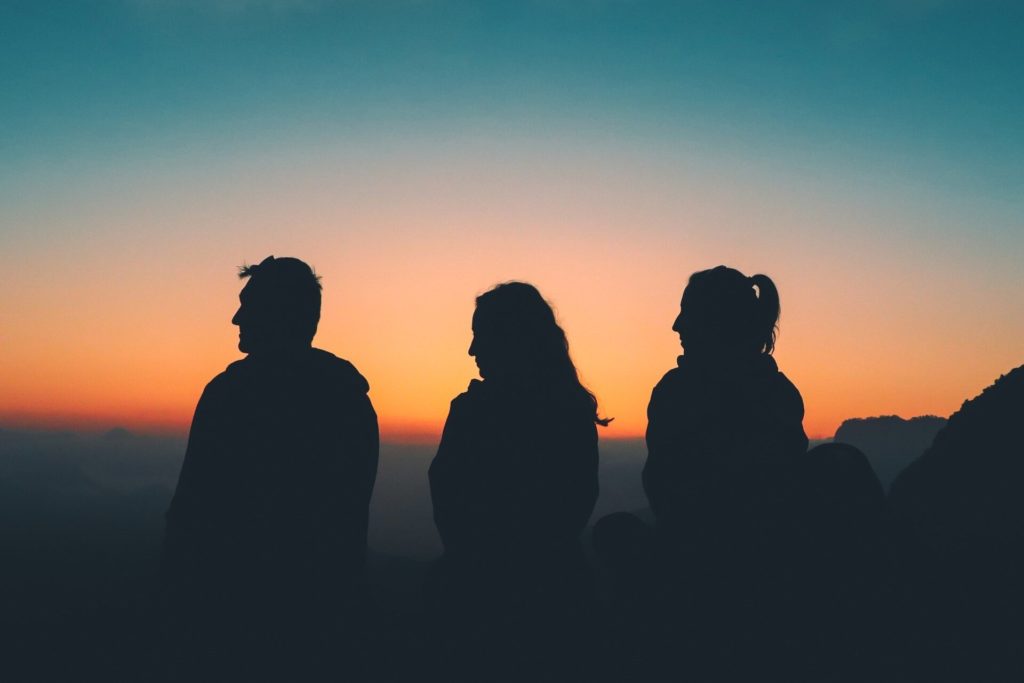Silhouetten von drei Personen beim Sonnenaufgang