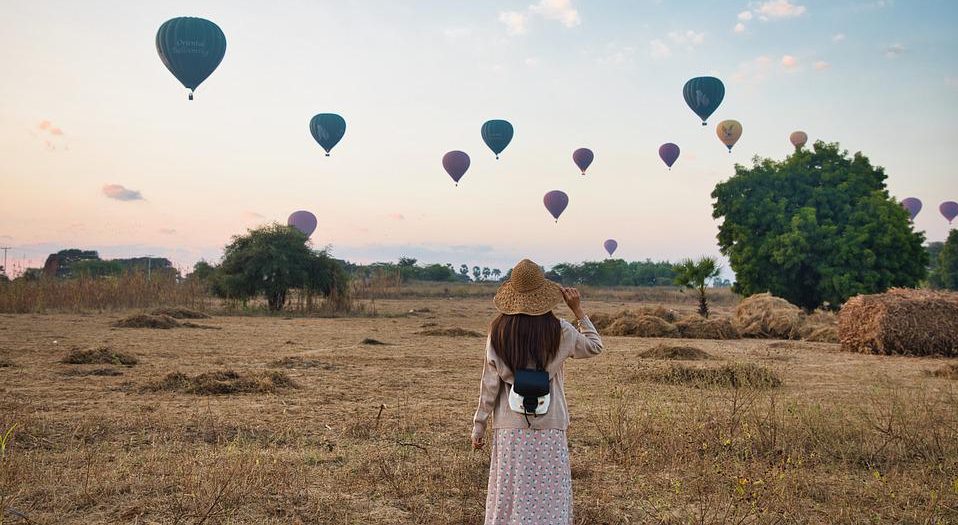 Frau von hinten auf einem Feld mit Heißluftballons im Hintergrund.